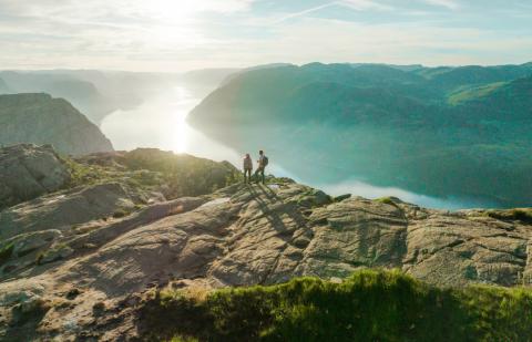 Two people standing on top of a cliff facing the water
